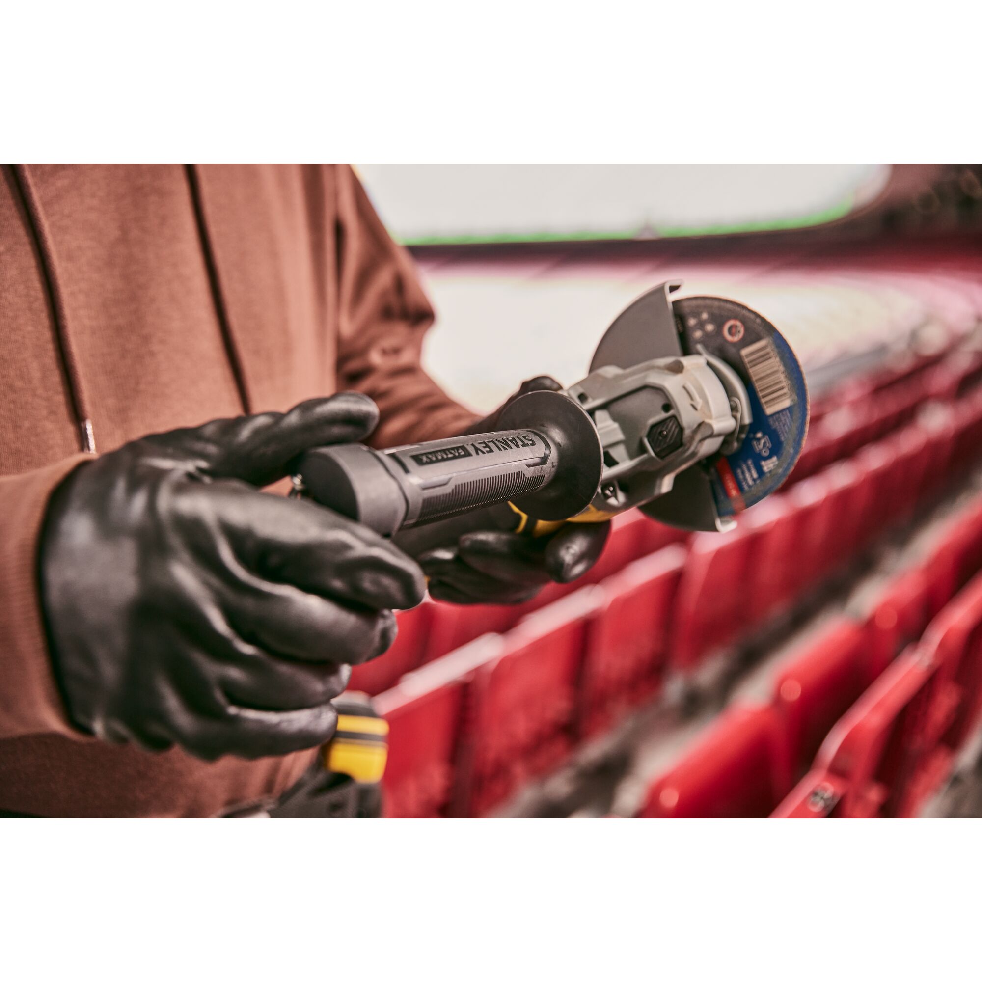 STANLEY SFMCG700M2K cordless angle grinder held by gloved hands in a stadium setting.